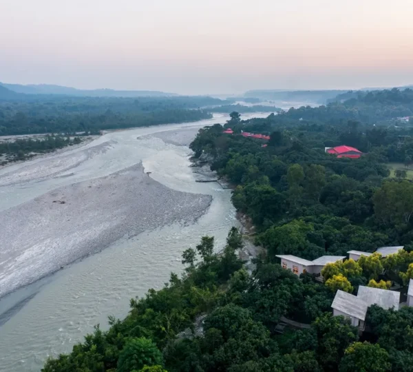Riverside resorts in Jim Corbett with an aerial view of the Kosi River, luxury cottages, and lush forest surroundings offering a peaceful nature escape.