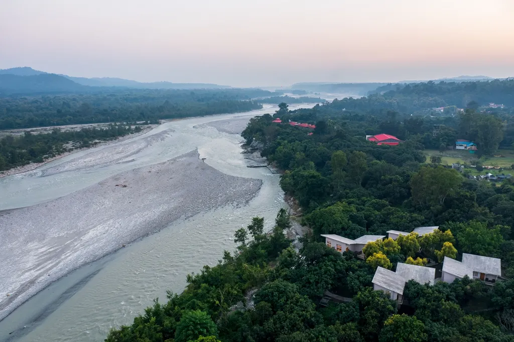Riverside resorts in Jim Corbett with an aerial view of the Kosi River, luxury cottages, and lush forest surroundings offering a peaceful nature escape.